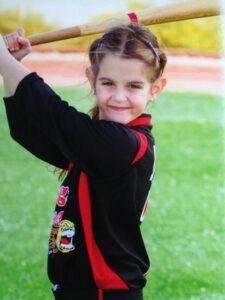 Jenna at around 7 years old holds a bat poised to hit the next pitch